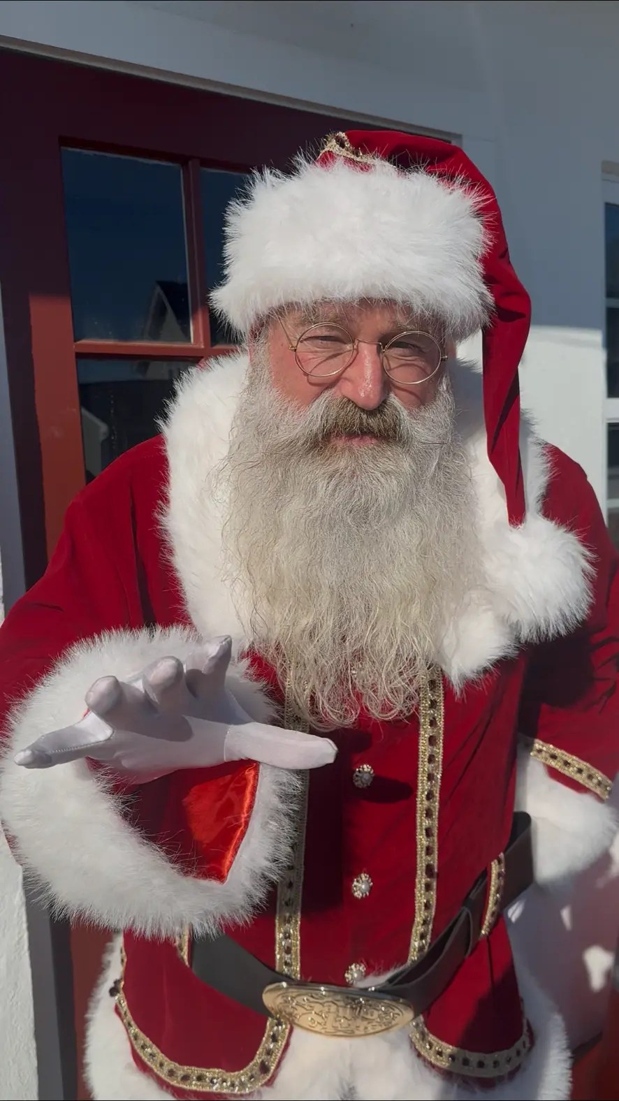 Santa in a gold-trimmed red suit reaching out a white-gloved hand in greeting