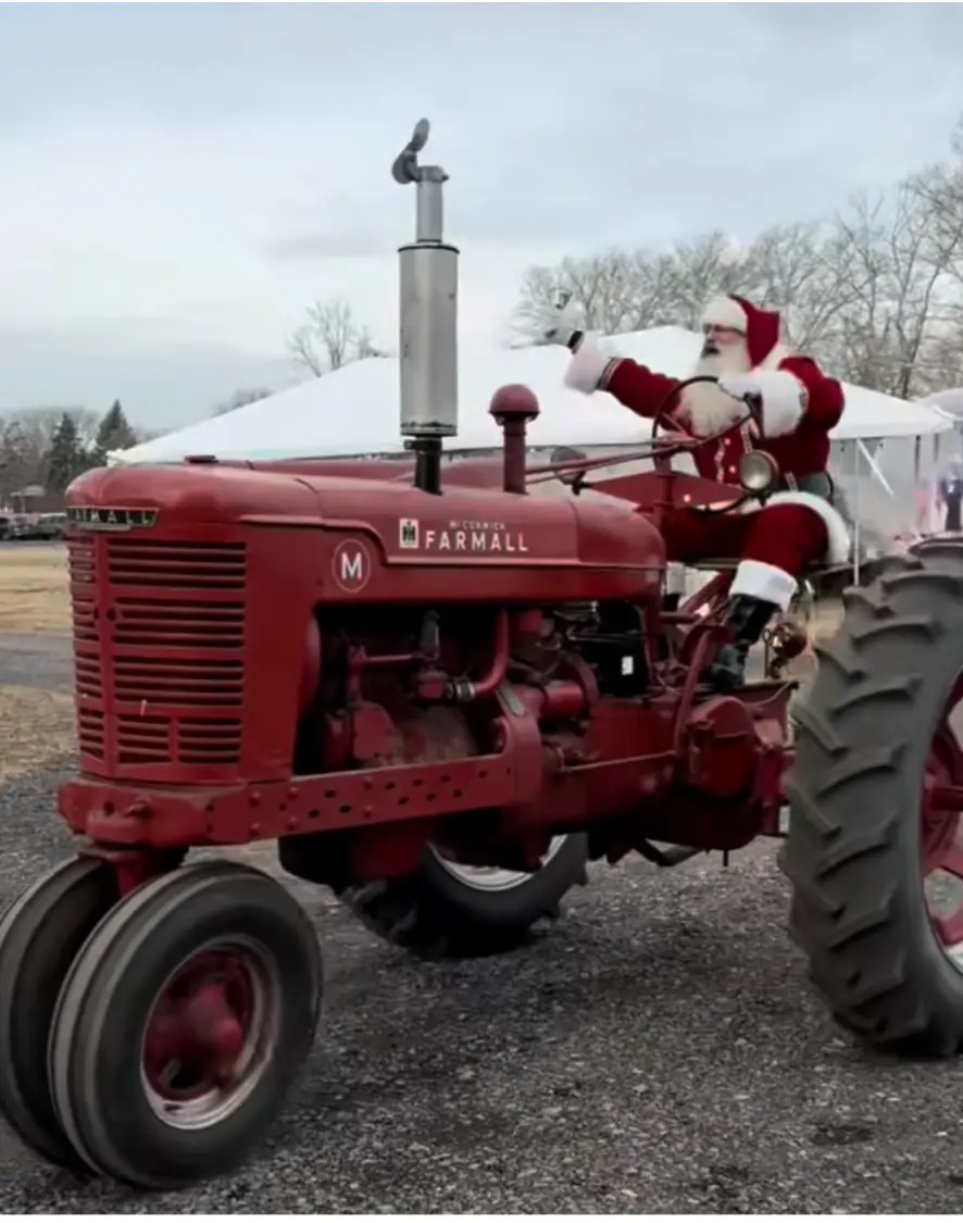 Santa waving from the seat of a red McCormick Farmall tractor at a winter event