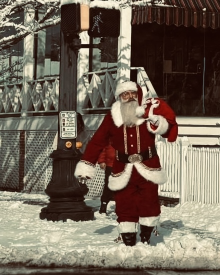 Santa standing at a snowy street corner beside a pedestrian crossing signal