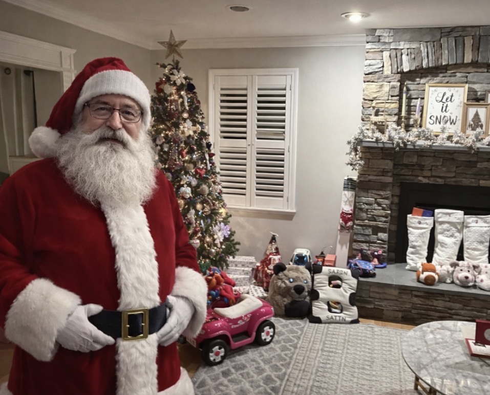 Santa standing beside a decorated Christmas tree in a family living room