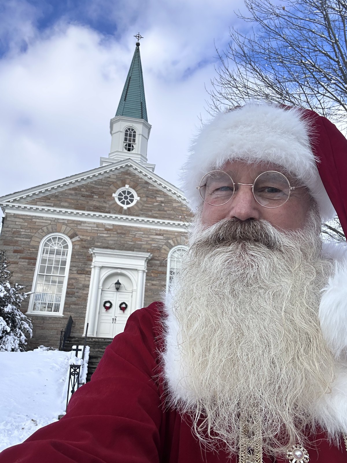 Santa outside a snow-covered stone church on a bright winter morning