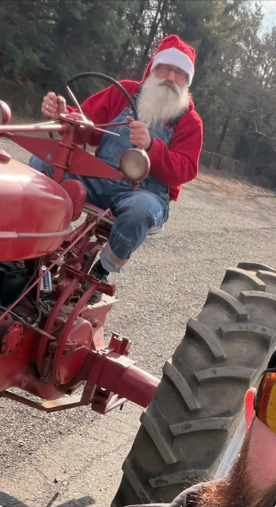 Santa in a red hoodie and overalls at the wheel of a vintage red tractor